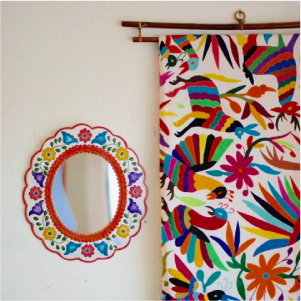 Photo of small painted, oval mirror and a large Otomí tablecloth hanging on the wall-Zinnia Folk Arts